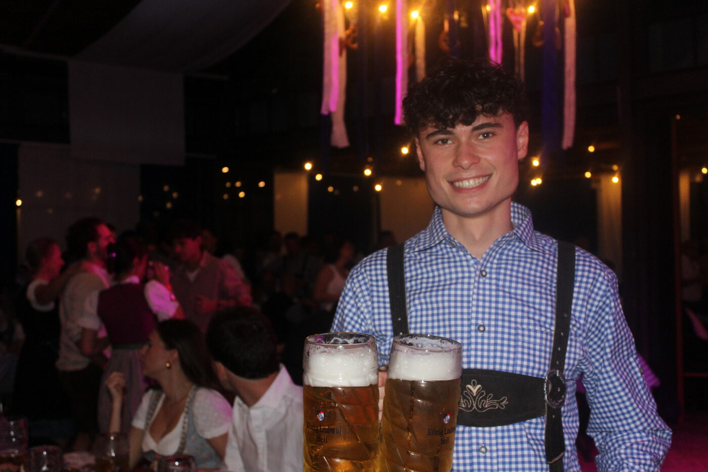 Lächelnder Kellner in Lederhose serviert zwei Maß Bier